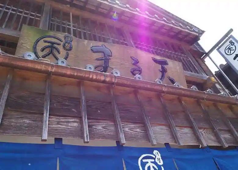 This picture shows a signboard for an Isoage store called Isoage-Maruten in Okage Yokocho. A wooden signboard with the word "Maruten" etched into it is hanging in front of the store.
