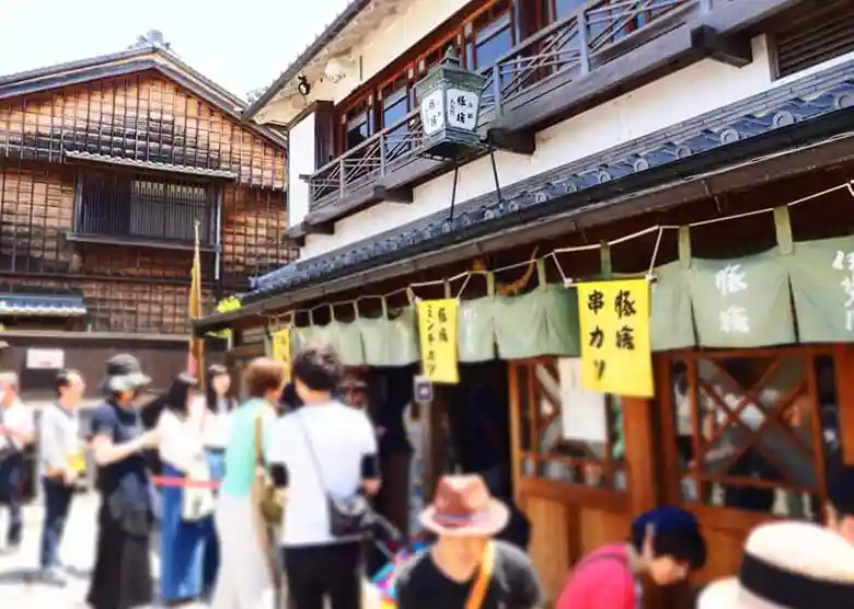This photo shows the storefront of a butcher shop called Butasute in Okage Yokocho. The storefront has a curtain with the words "Butasute" and "Deep-fried skewers" written in black letters on a yellow cloth.