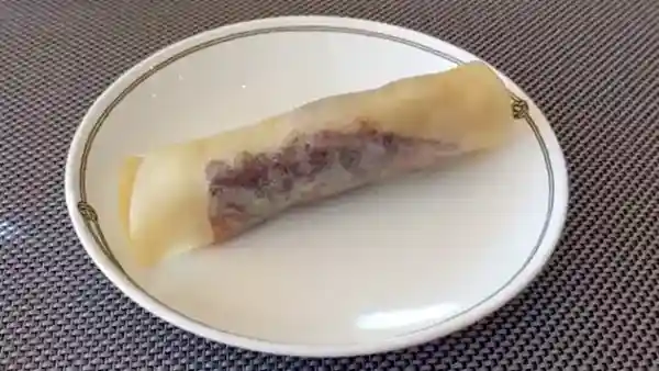 This photograph depicts a Peking duck served on a white plate. The dish features the duck and its ingredients wrapped in white skin, measuring about 12 cm in length.