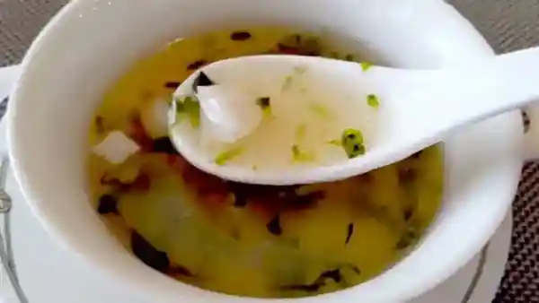 This photograph depicts seafood and aosa (sea lettuce) soup served on a white plate. The clear broth is filled with green aosa and white scallops.