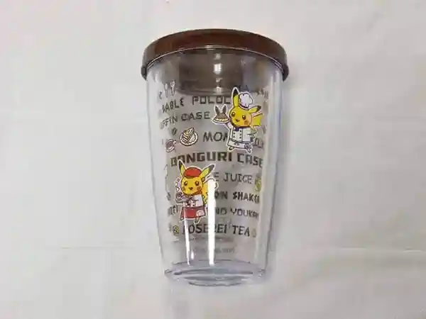 This photograph depicts the original cup from the Pokemon Cafe. As you can see, the cup previously contained Cola, but it has since been consumed, leaving it empty. The surface of the cup features illustrations of Chef Pikachu and Waitress Pikachu. The mug is made of plastic, but its double-layered structure helps to maintain a consistent temperature for the drink.