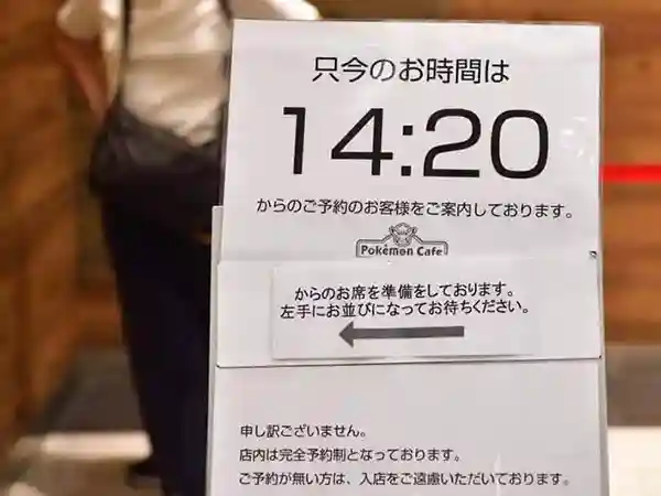 This photograph displays a sign in front of the Pokémon Café that provides information about reservations. At this time, customers who made reservations for 2:20 p.m. are being directed inside. Please note that the Pokémon Café is a reservation only.