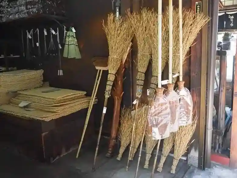 The photo shows brooms made of bamboo and rugs woven of straw lined up in front of Naito Shoten.