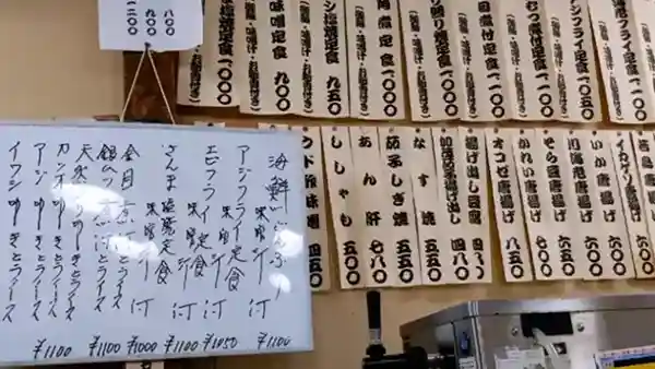 This photograph shows a wall inside the Sanshu-ya Ginza Store with several menus posted. The set menus of the day are written on a whiteboard, and you can choose from options such as a seafood rice bowl, fried horse mackerel, fried shrimp, grilled salt-crusted Akinoto fish, simmered Red bream, simmered Patagonian toothfish, and sashimi. The set menus are priced at 1,050 yen for the fried horse mackerel and 1,010 yen for the other options.
