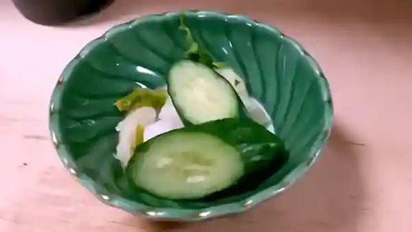 This photograph depicts pickled cucumber and turnip, with rice bran as the pickling agent. The ingredients are served on a green plate.