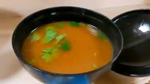 This picture depicts miso soup served in a black bowl. The ingredients include nameko mushrooms and tofu. The surface of the soup is garnished with Japanese parsley.