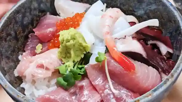 This picture shows a Sashimi rice bowl served in a bowl of rice with thick slices of sashimi. Sashimi includes tuna, bonito, yellowtail, salmon roe, squid, octopus, and sweet shrimp.