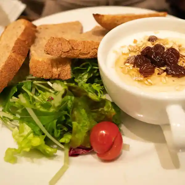 This photo shows the Granola & Yogurt Plate Set. It consists of a salad, four slices of toast, and a white cup with granola and yogurt on a white plate. The toast is whole grain bread called "Whole Grain Seikatsu" This bread is baked with whole wheat flour from Haruyokoi wheat grown in Hokkaido.