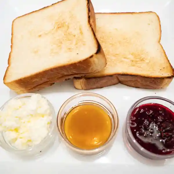 This photo was taken of "Daily bread " hana. Two thick slices of toast and three kinds of confiture are served on a white plate. The confiture comes in a clear glass container. The three types of confiture are homemade raspberry jam, whipped butter, and maple syrup.
