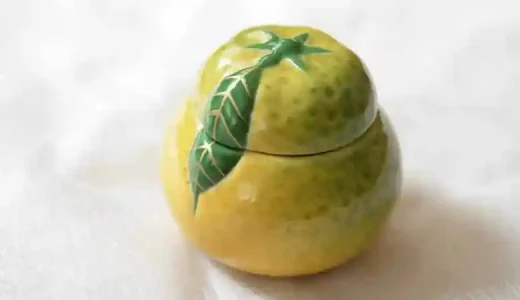 This photo shows a ceramic container for yuzu miso. Yuzu miso is a mixture of miso and yuzu peel or juice. The container is shaped like a yuzu (Japanese citron). The surface is yellow, the same color as the yuzu, and is decorated with yuzu leaves. It is 5 cm in diameter and 5 cm high.
