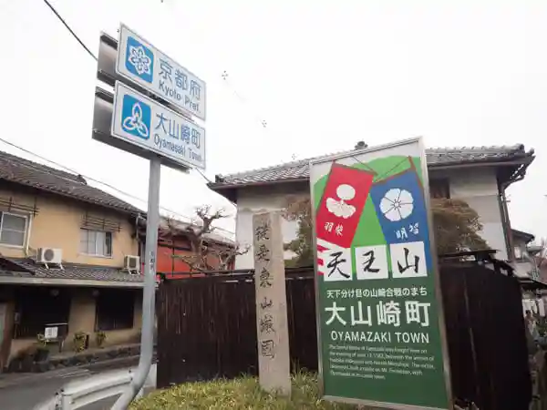 This photo shows a signboard at the border between Osaka and Kyoto prefectures. The words "Kyoto Prefecture" and "Oyama Town" are printed in blue letters on white metal.