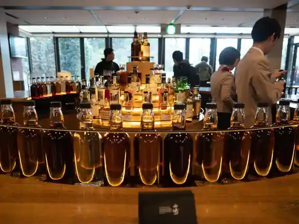 This photo shows the tasting counter at the Whiskey Museum of Suntory Yamazaki Distillery. Two waitstaff, a man and a woman, are serving whiskey.