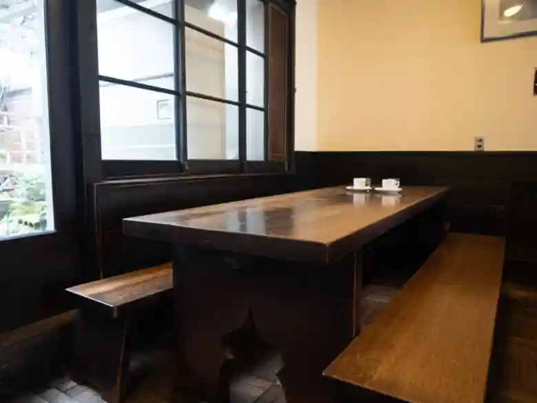 This photo shows the interior of the cafe. Tables and couches made of oak wood lined the interior. They are the work of Tatsuaki Kuroda, a living national treasure. The shiny black grain of the tables gave a sense of history. The high ceiling and quiet atmosphere make it feel like a classroom.