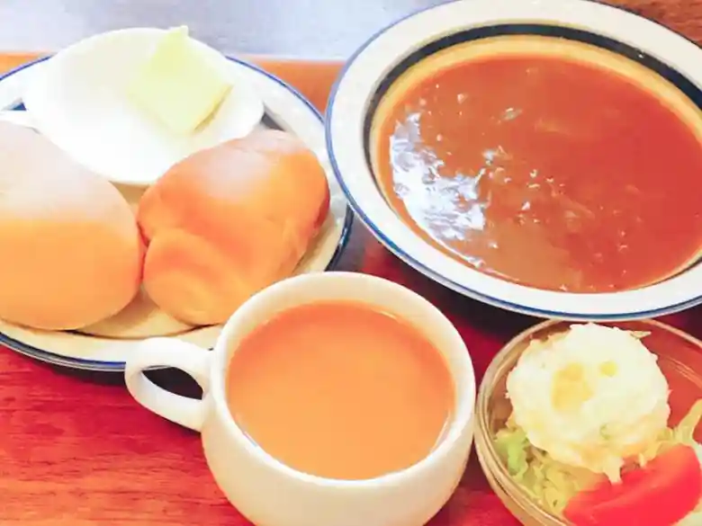 This photo shows the curry bread set. It consists of curry in a dish instead of curry bread, two pieces of oval-shaped bread, a salad, and a drink.