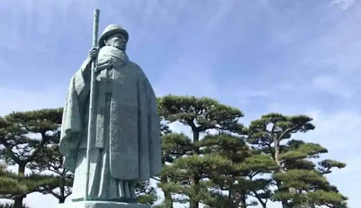 This photo shows a bronze statue of Kokichi Mikimoto at Mikimoto Pearl Island in Toba, Japan. The figure is depicted wearing a bowler hat and cloak and holding a cane in his right hand.