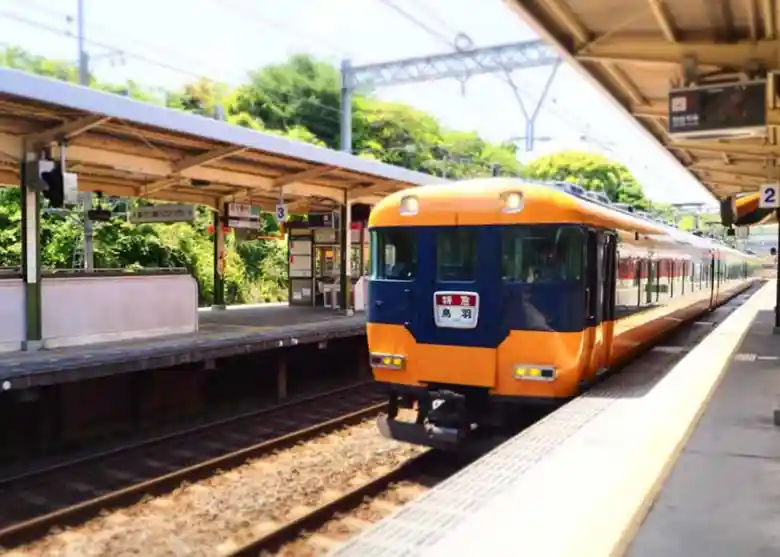 This photo shows a Kintetsu limited express train heading to Toba. A car with an orange-painted body is stopped at the station platform.