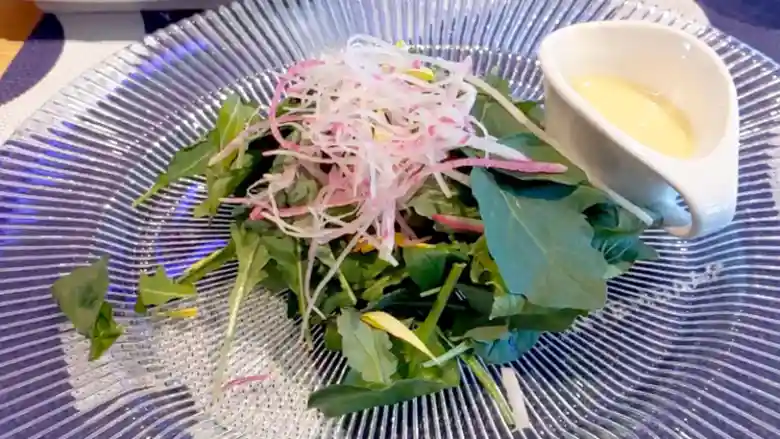 彩りカブ大根サラダの写真です。青い縞模様が入ったガラスの皿に盛られています。葉野菜の緑色と根菜の白と紫色が華やかで彩りが鮮やです。