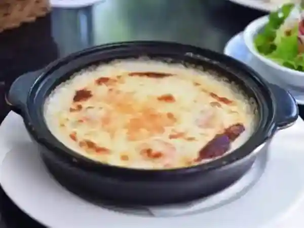 This photograph shows the gratin being served in its original black flat pan, which has a diameter of approximately 15 cm. The cheese on the surface of the gratin is burnt.