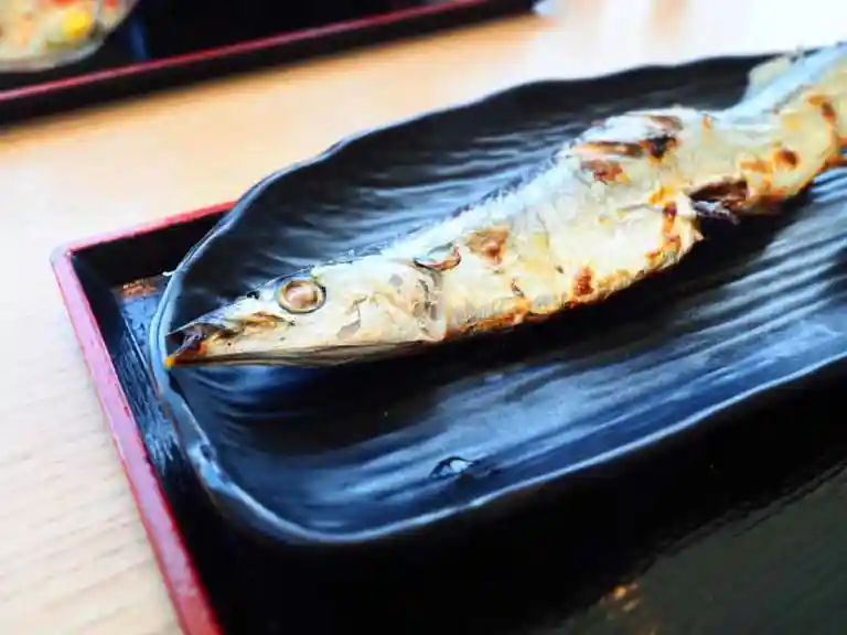 秋刀魚の塩焼きの写真です。黒い皿に表面が焦げた秋刀魚の頭側半分が写っています。北海道釧路産の新秋刀魚です。