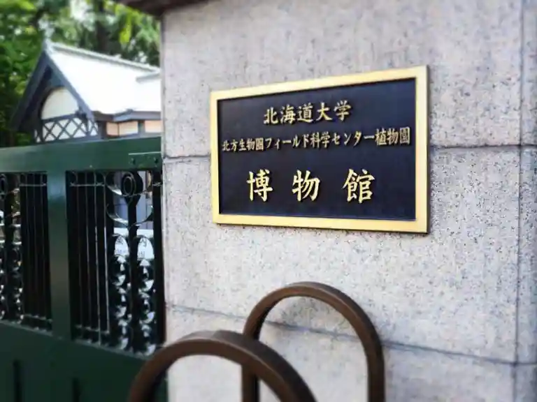 北海道大学植物園の入り口の写真です。黒い板に、北海道大学博物館、北方生物園フィールド科学センター植物園と銀色の文字が刻まれています。
