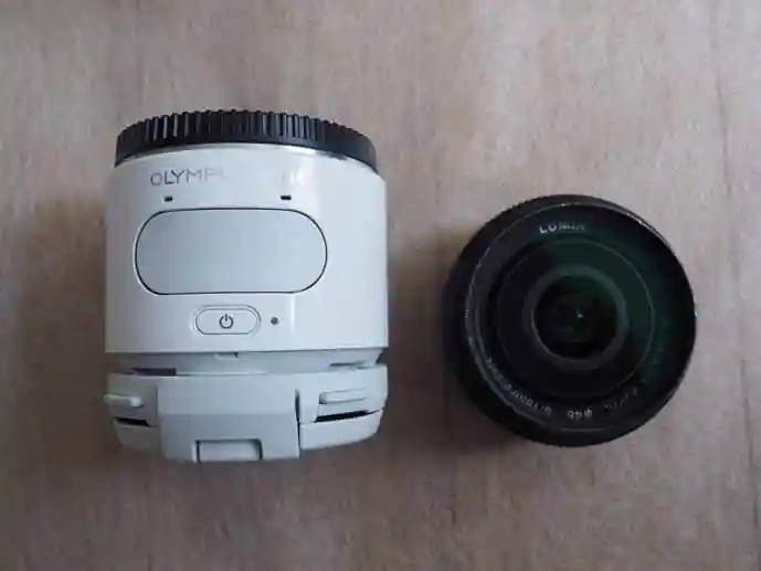 OLYMPUS AIR A01というカメラの画像です。直径57mm、長さ57mmの円筒形をした白いカメラです。