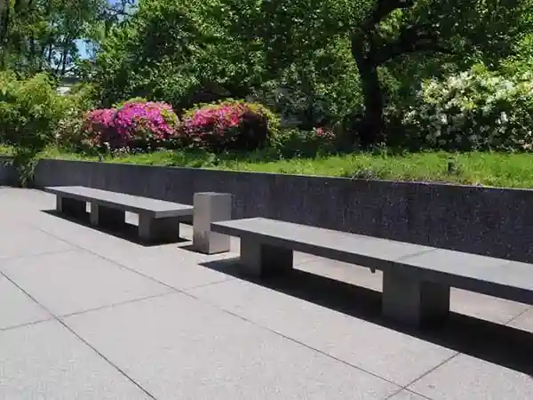 This photo depicts stone benches in front of the Gallery of Horyuji Treasures. In the background, there are trees and red flowers behind the courts.