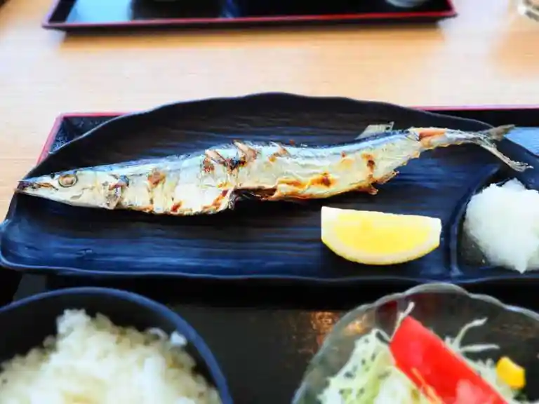 秋刀魚の塩焼き定食の写真です。黒い皿の上に焼かれた秋刀魚が乗せられています。秋刀魚の横にはレモンと大根おろしが添えられています。