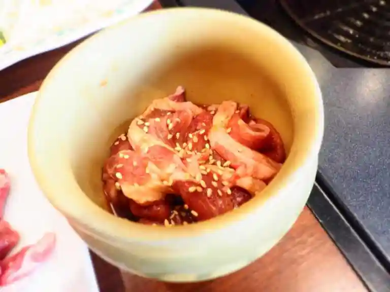 漬け込みラムの写真です。壺の中にタレに漬けたラム肉が名行っています。ゴマがふられています。