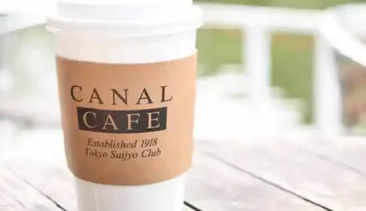 牛込壕に面したデッキサイドのテーブルに置かれたコーヒーのカップの写真です。白いプラスチック製で中央に薄茶色のラベルがはられています。ラベルには濃い茶色の文字で「CANAL CAFE」と書かれています。