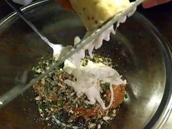 鶏ひき肉と砕いた椎茸、刻んだニラが入ったガラス製のボールに、すり下ろしたやまといもを加えている写真です。