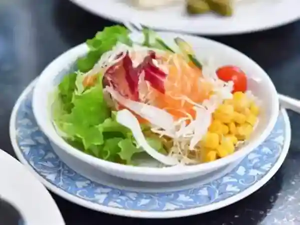 This photograph shows a salad served on a round white plate. The salad contains the ingredients of lettuce, cabbage, small tomatoes, and corn.