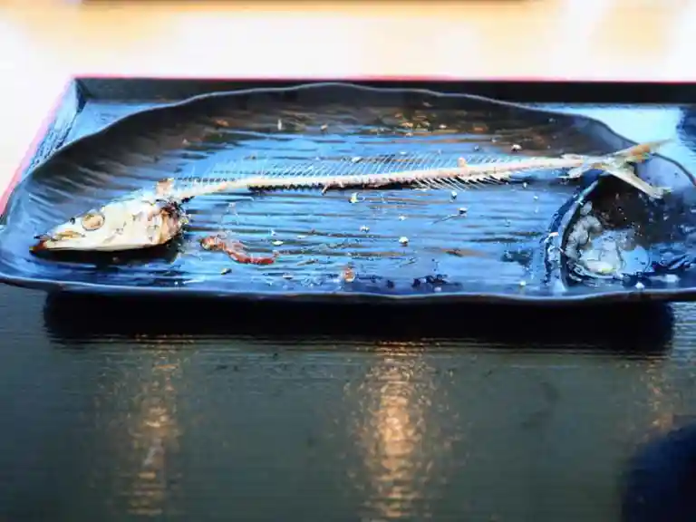 食べ終わった秋刀魚の写真です。黒い皿の上に頭と骨だけが残っています。
